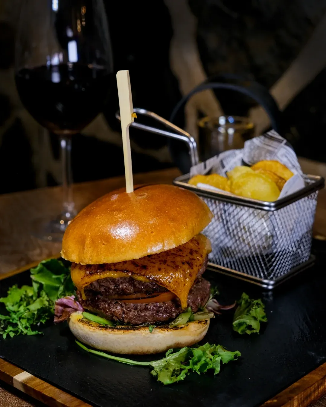 Hamburguesa de angus con cheddar fundido y patatas, con una copa de tinto