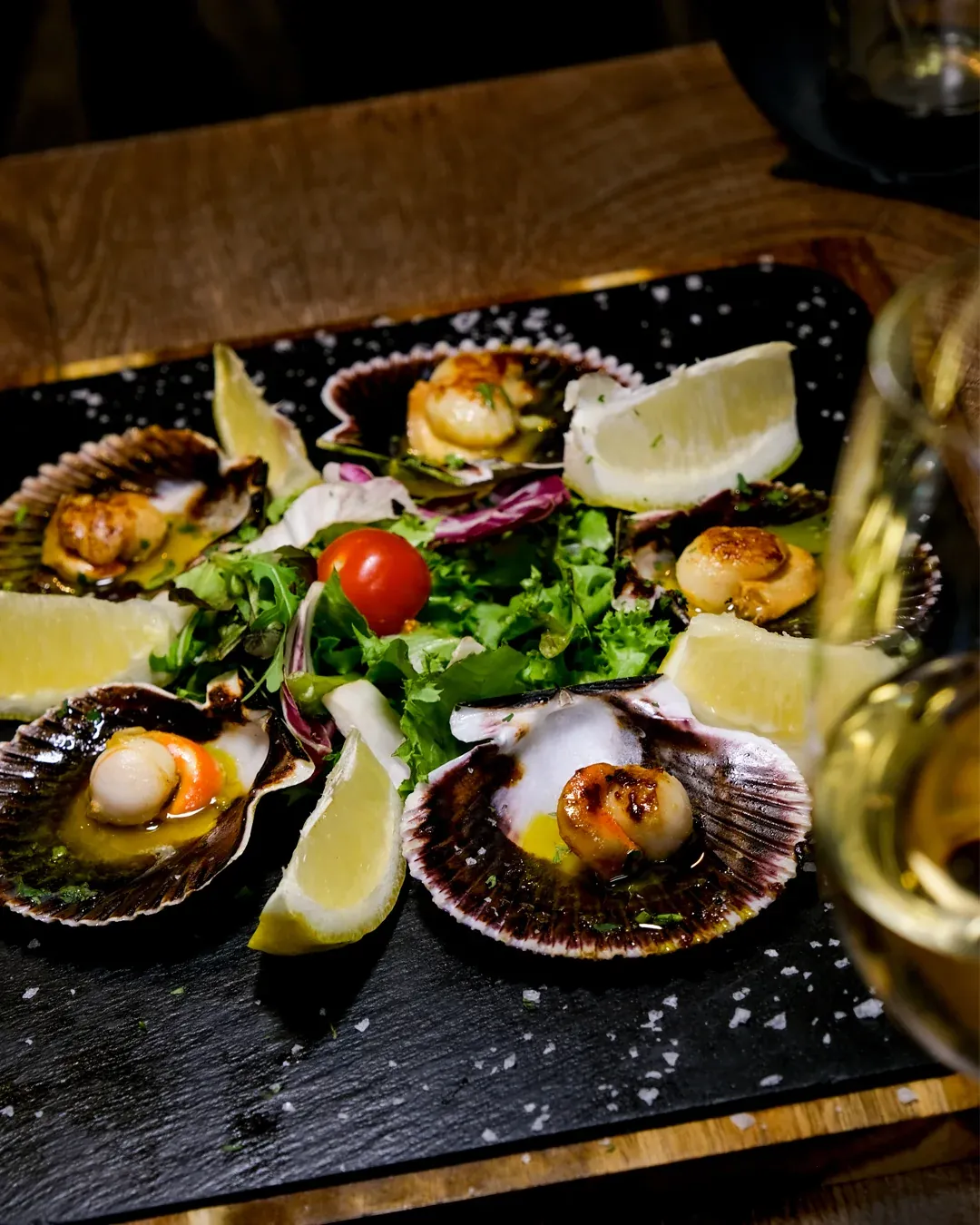 Zamburiñas a la plancha sobre pizarra con limón y una copa de vino blanco